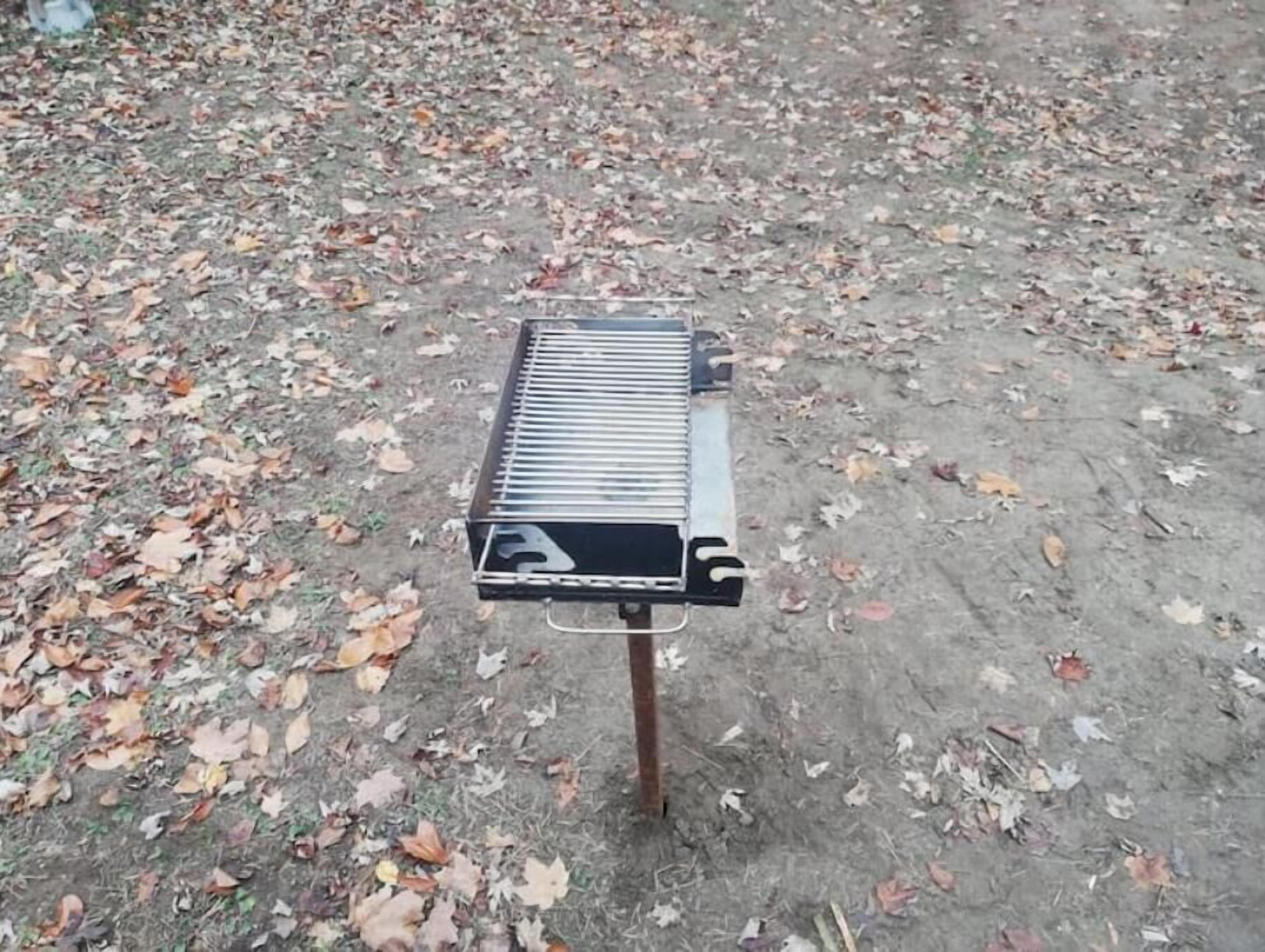 A portable grill on a dirt surface with scattered leaves.