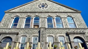A large stone building with a triangular pediment and multiple arched windows. - Stunning, historic holiday apartment  (Criccieth)