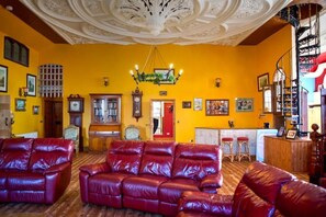 Ein Zimmer mit gelber Wand, einem roten Ledersofa, einem Holzkabinett und einer Chandelier.