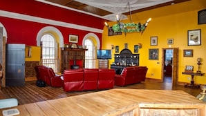 A spacious room with a wooden floor, red and yellow walls, a fireplace, and a television. - Stunning, historic holiday apartment  (Criccieth)