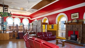 A spacious living room with red leather sofas, a fireplace, and a staircase leading to an upper level. - Stunning, historic holiday apartment  (Criccieth)