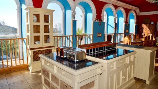 A kitchen with a central island, white cabinetry, and a view through large arched windows. - Stunning, historic holiday apartment  (Criccieth)