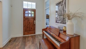 Un pasillo con una puerta de madera, un piano y un cartel enmarcado en la pared.