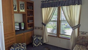 A room with a wooden cabinet, a television, a patterned ottoman, and a window with curtains. - Park unit #3 for rent by Silver Lake NY  (Perry)