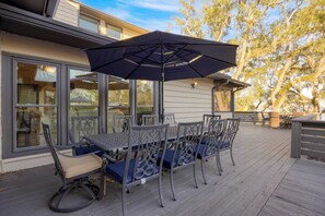 Una terraza con una mesa y sillas, un paraguas grande y un edificio con ventanales grandes al fondo.