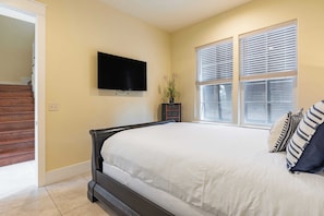 A bedroom with a bed, a TV mounted on the wall, a window with blinds, and a staircase leading to another room. - Amalfi Breeze by Avantstay Walk to the Beach, Luxe Design (Miramar Beach)