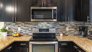 A modern kitchen with dark cabinets, a stainless steel microwave, a built-in oven, and a coffee maker.
