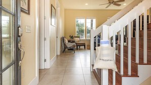 A hallway with a staircase, a door with a handle, a ceiling fan, and a bag with "AVANTSTAY" written on it.