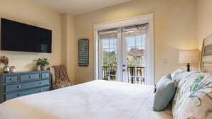 A bedroom with a large bed, a dresser, a flat-screen TV, a balcony with a view, and a motivational quote on the wall.