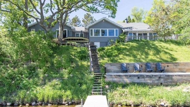 Une maison dotée d’une terrasse en bois, d’un escalier en pierre et d’une jetée qui s’avance dans un ruisseau.