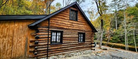 A log cabin with a gabled roof, two windows, and a stone foundation.
