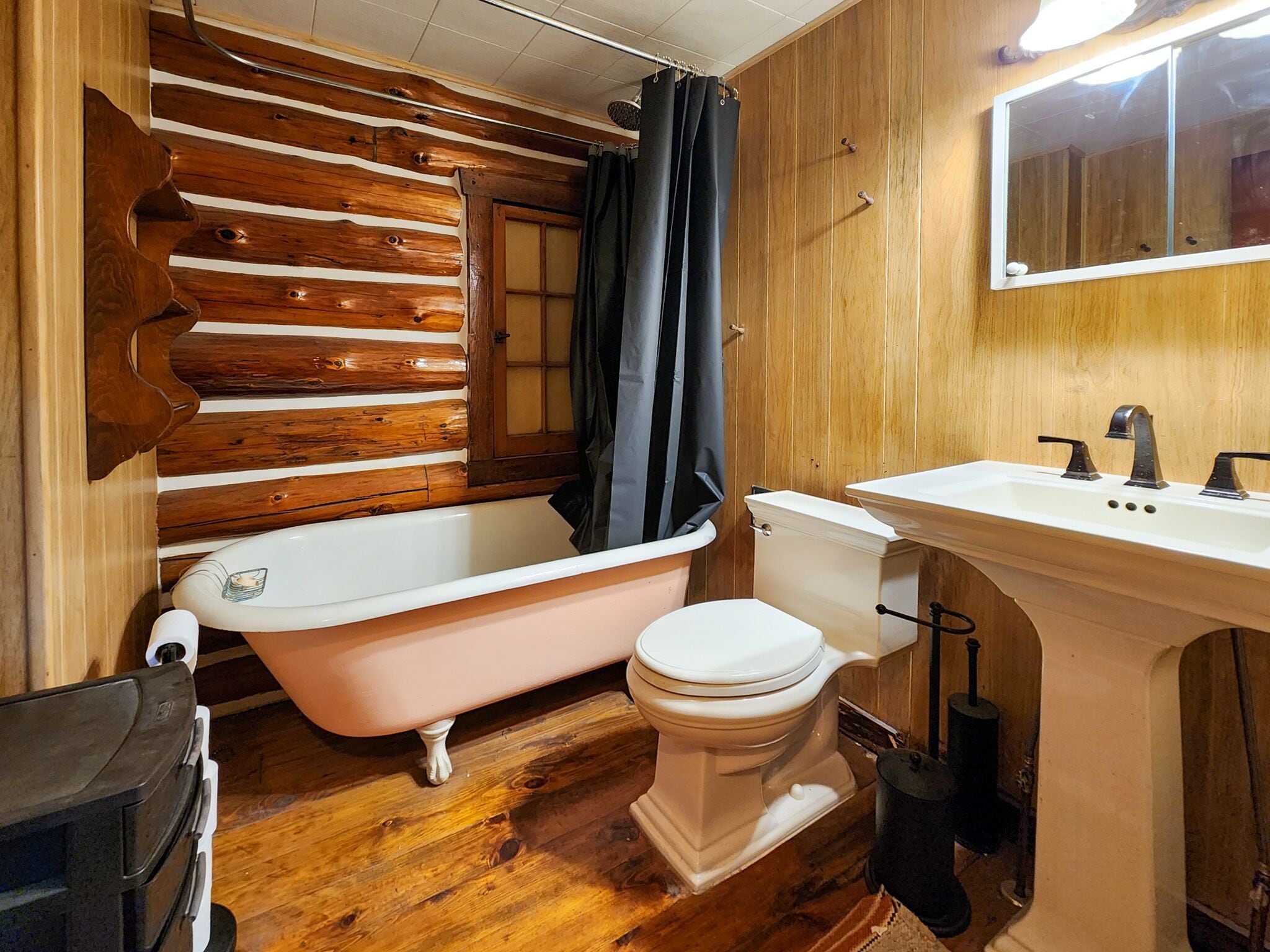 A bathroom with a wooden wall, a clawfoot bathtub, a toilet, and a sink with a mirror above it.