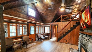 A log cabin interior with a wooden staircase, stone fireplace, and multiple seating areas. - Modern Luxury Meets Rustic Charm - Cozy Log Cabin (East Stroudsburg)