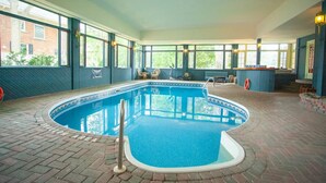 An indoor swimming pool with a tiled edge, surrounded by brick flooring and large windows.