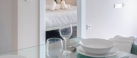 A hotel room with a bed, a glass table with a salad, wine glasses, and a TV on the wall.