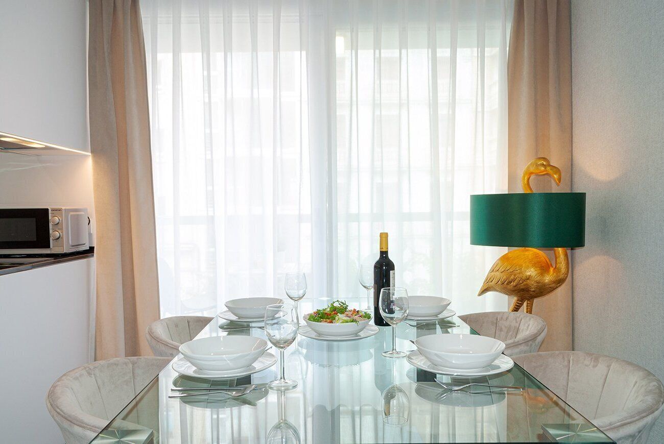 A dining area with a glass table, white plates, and a bottle of wine.