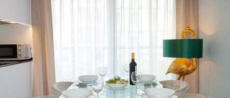 A dining area with a glass table, white plates, and a bottle of wine.