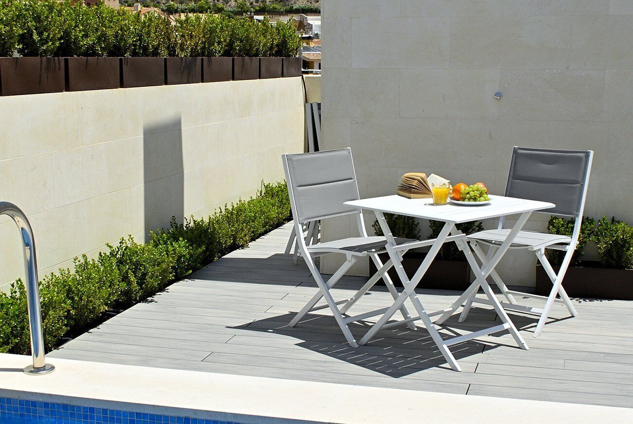 An outdoor patio with a pool table, two chairs, and a table set with fruit and a drink.