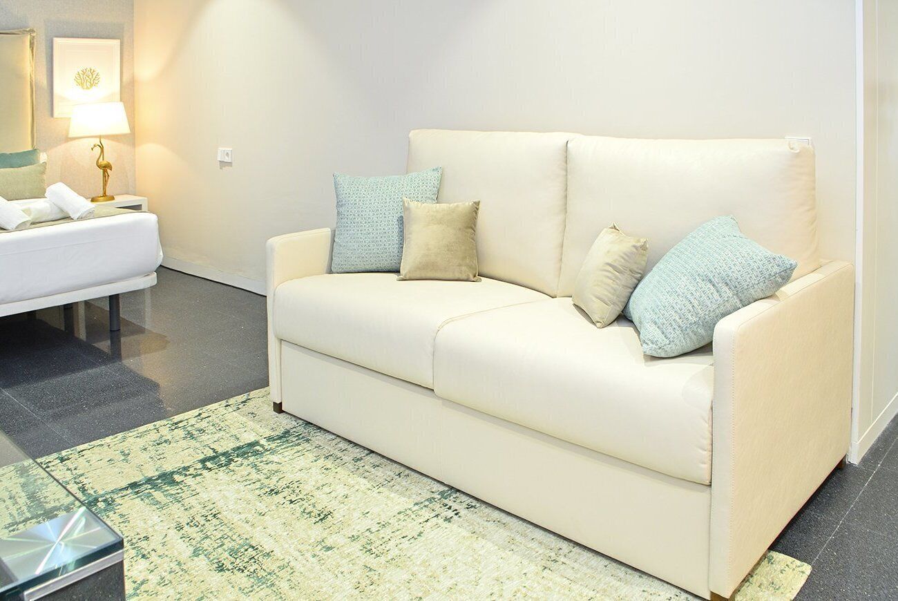 Een moderne woonkamer met een beige bank, een tapijtend met een patroon en een kleine tafel met een lamp.