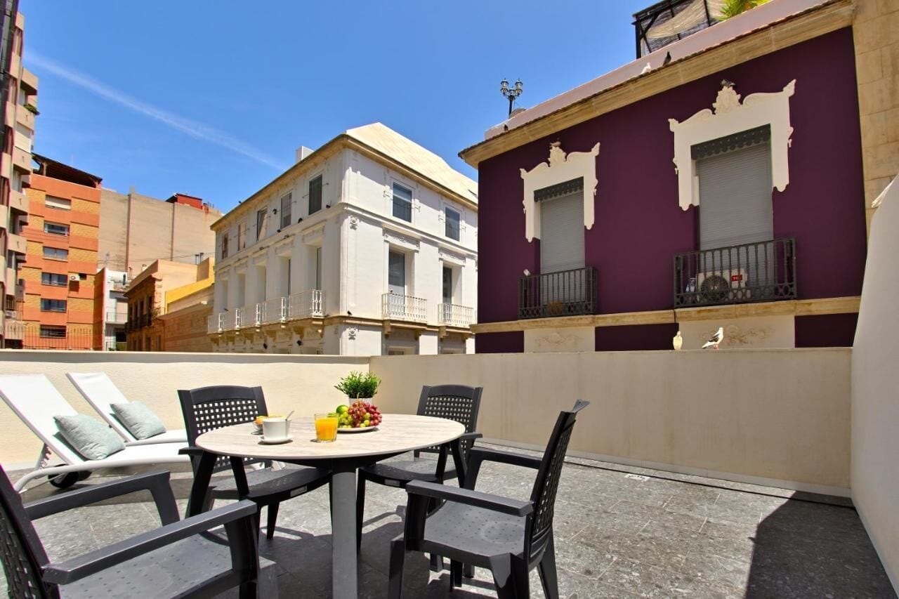 A rooftop terrace with a round table, black chairs, and a small garden.