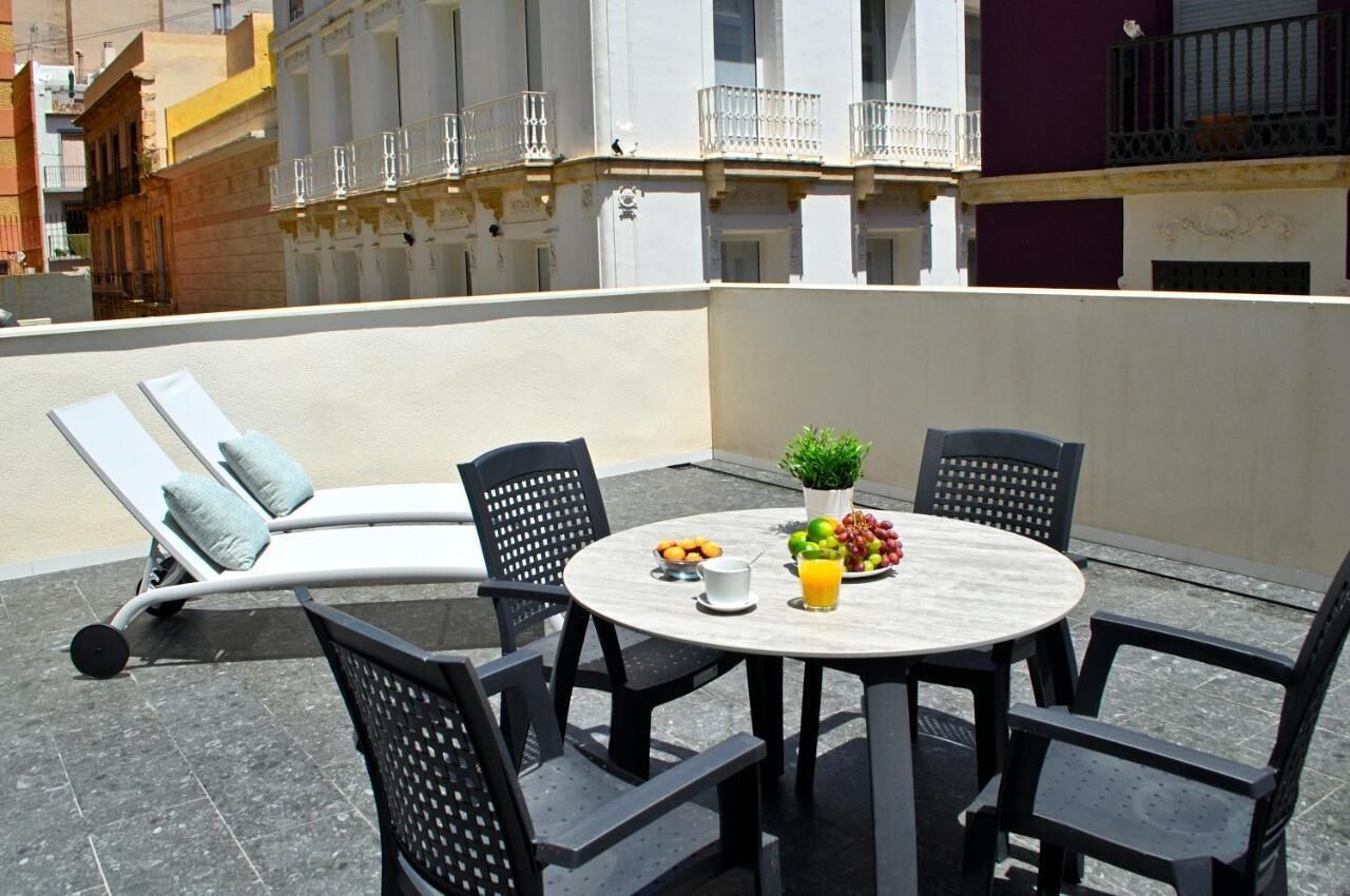Une terrasse sur le toit avec une table ronde, quatre chaises, un fauteuil et une petite plante en pot.