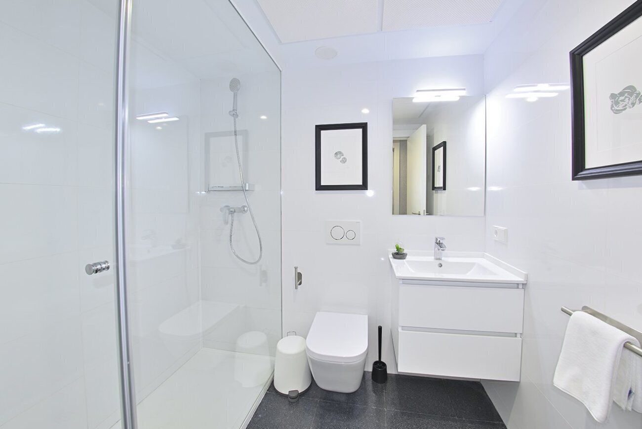 Un baño moderno con cabina de ducha de vidrio, inodoro blanco, lavamanos con espejo y un cuadro en la pared.
