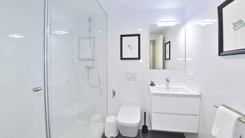 Een moderne badkamer met een douchecabine van glas, een wit toilet, een wastafel met spiegel en een lijst met een afbeelding aan de muur.