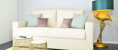 A white sofa with two cushions, two gold-rimmed side tables, and a golden floor lamp with a blue lampshade.