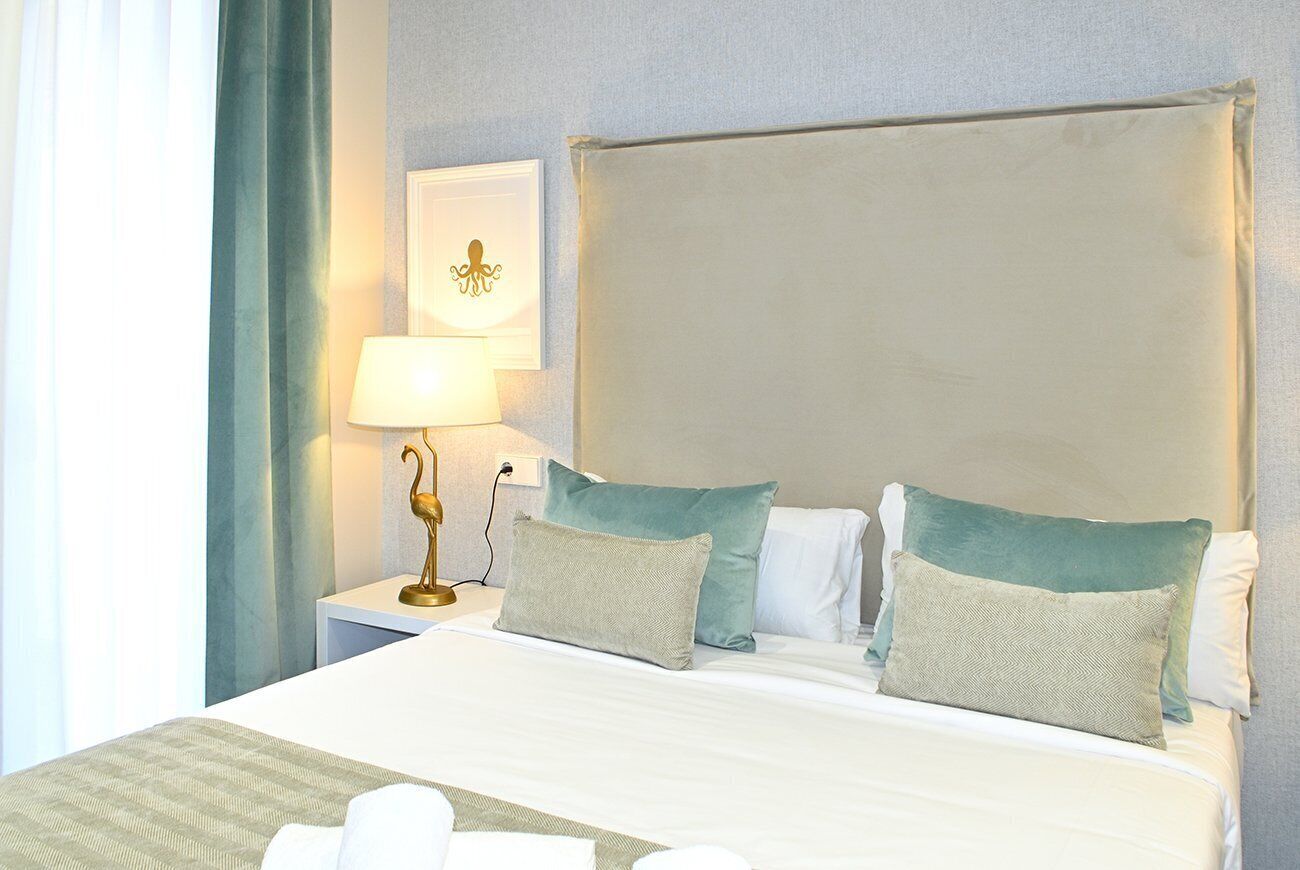 A hotel room with a large bed, two pillows, a nightstand with a lamp, and a wall-mounted picture.