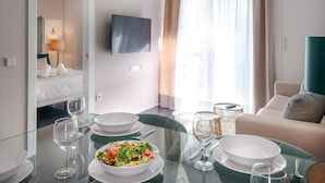 Habitación de hotel moderna con comedor, cama, televisor y vistas al exterior.