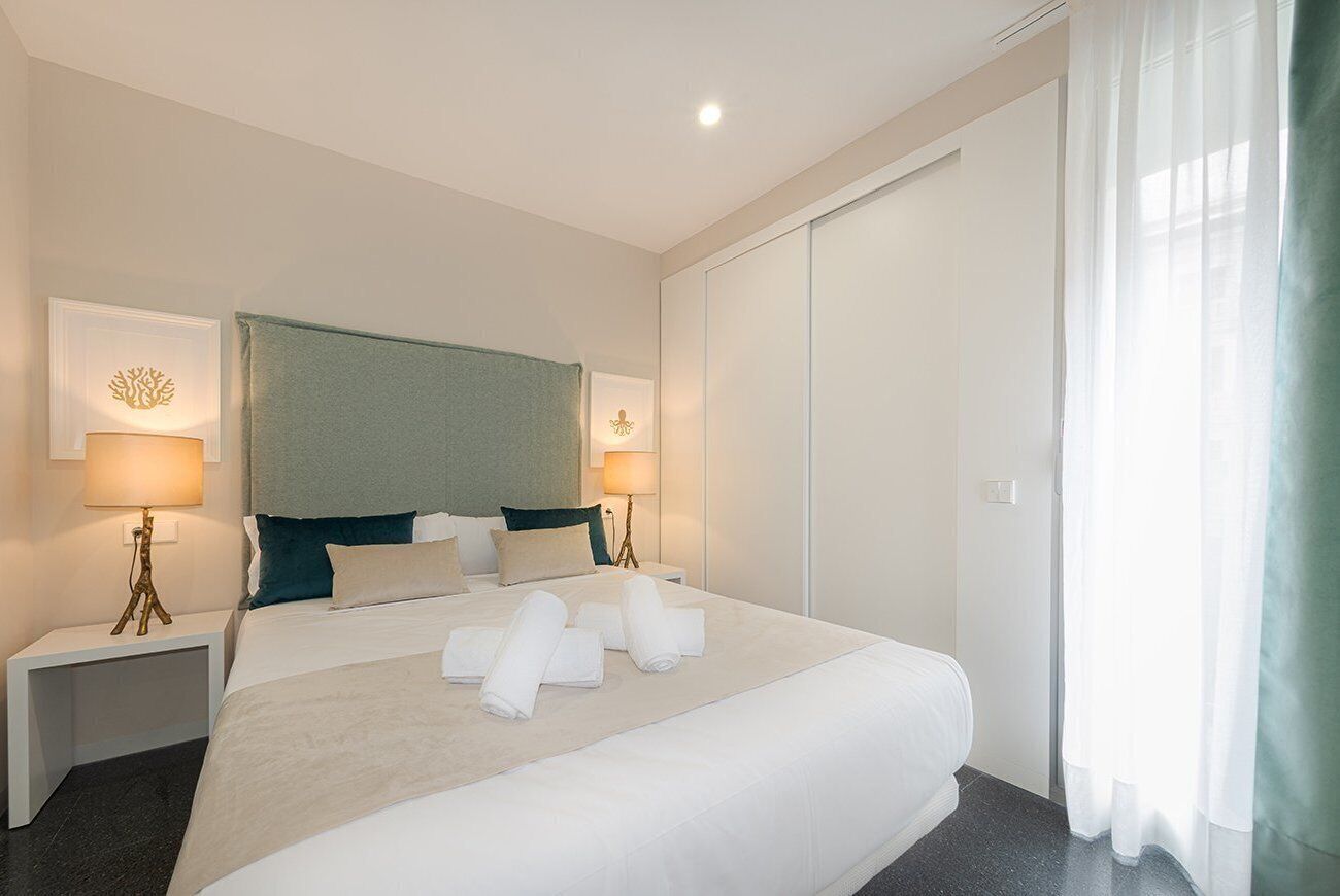 Una habitación de hotel con una cama grande, dos mesitas de noche con lámparas, un cabecero y un armario.