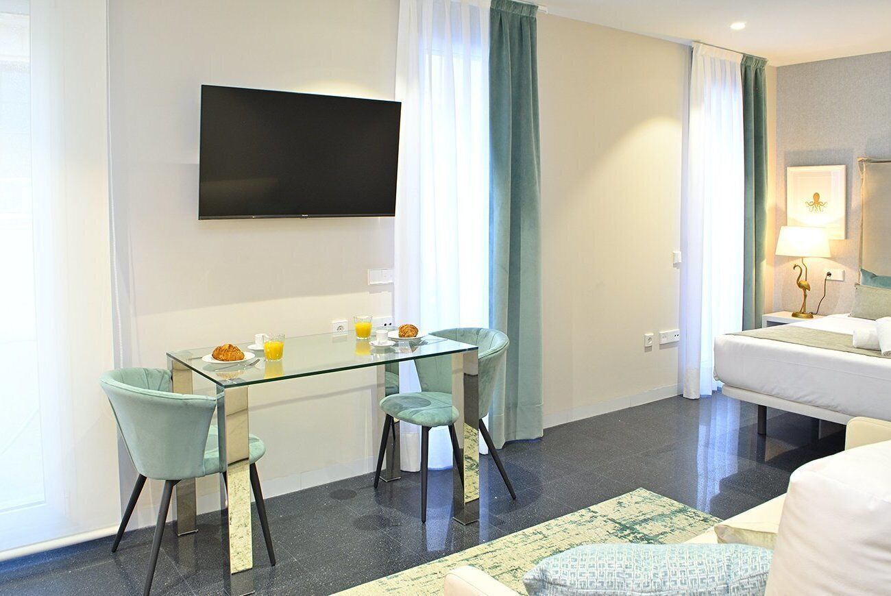 Una moderna camera d'albergo con un tavolo in vetro, due sedie, una televisione a schermo piatto, un letto e un comodino con una lampada.