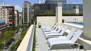 Zona de piscina en la azotea con sillones de descanso y una piscina, rodeada de edificios.