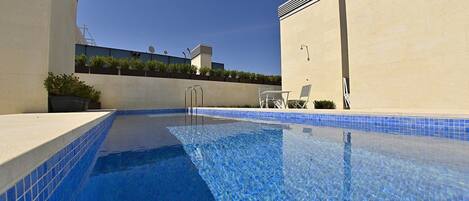Una piscina con acqua cristallina e blu, circondata da pareti beige e un bordo piastrellato.