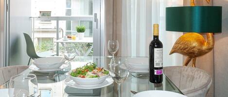 A dining area with a glass table, white plates, and a bottle of wine.