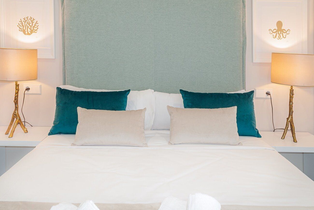 A neatly made bed with white and teal pillows, two bedside lamps, and wall art depicting sea creatures.