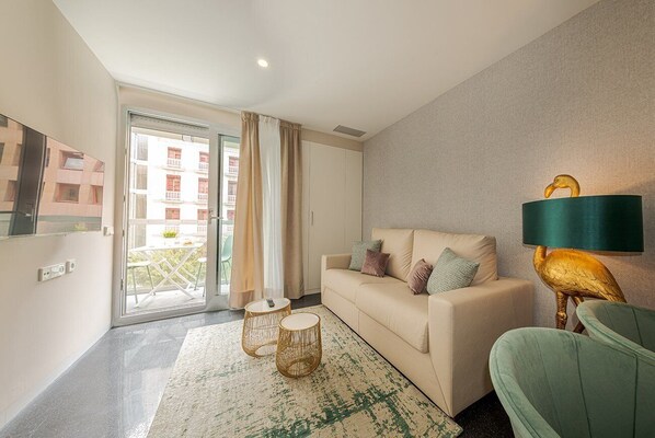 A modern living room with a sofa, a lamp, and a view through a glass door. - HoliHome Rambla 24 (Alicante)
