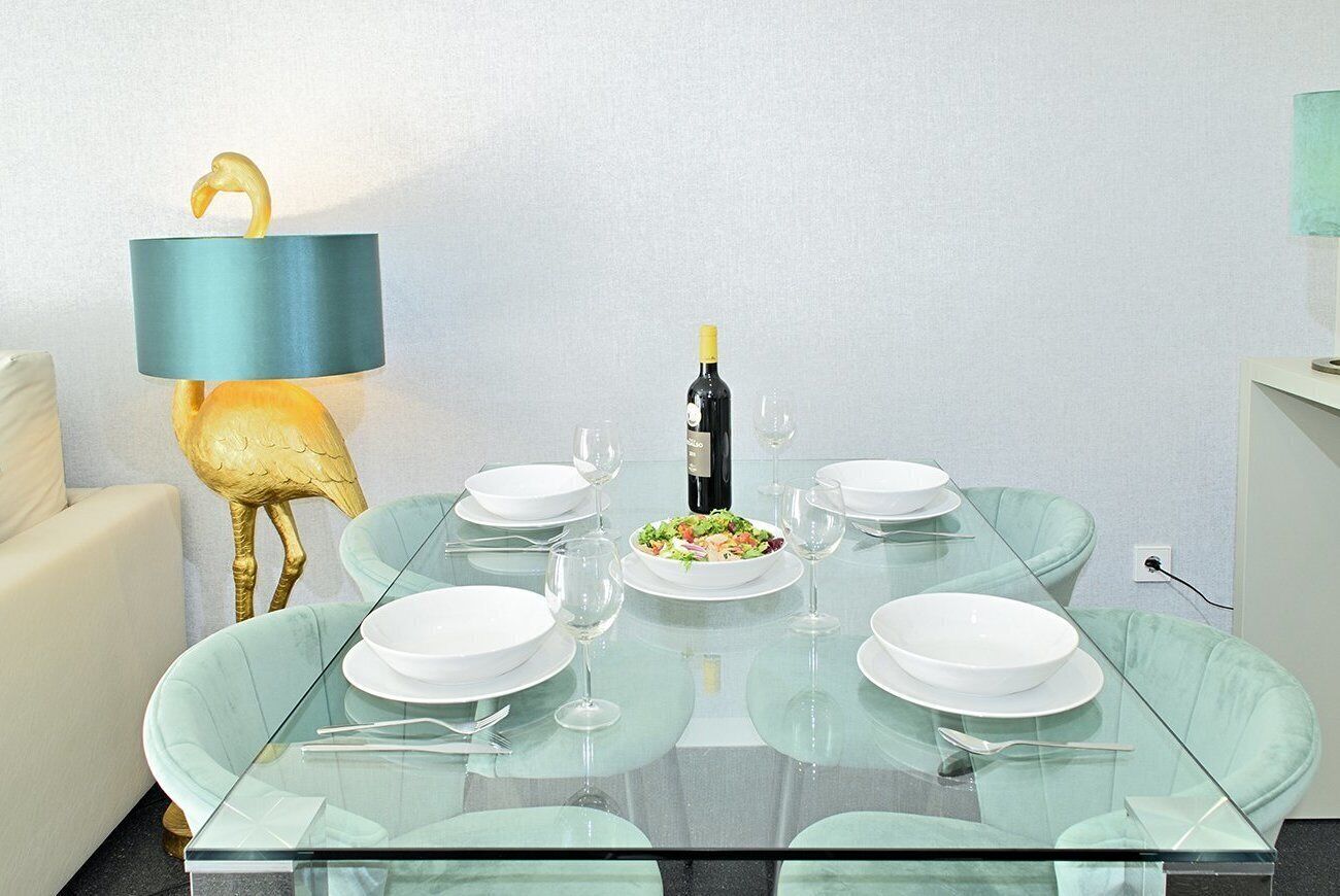 Une table à manger avec un plateau en verre, entourée de chaises, une bouteille de vin et une salade posées sur la table.