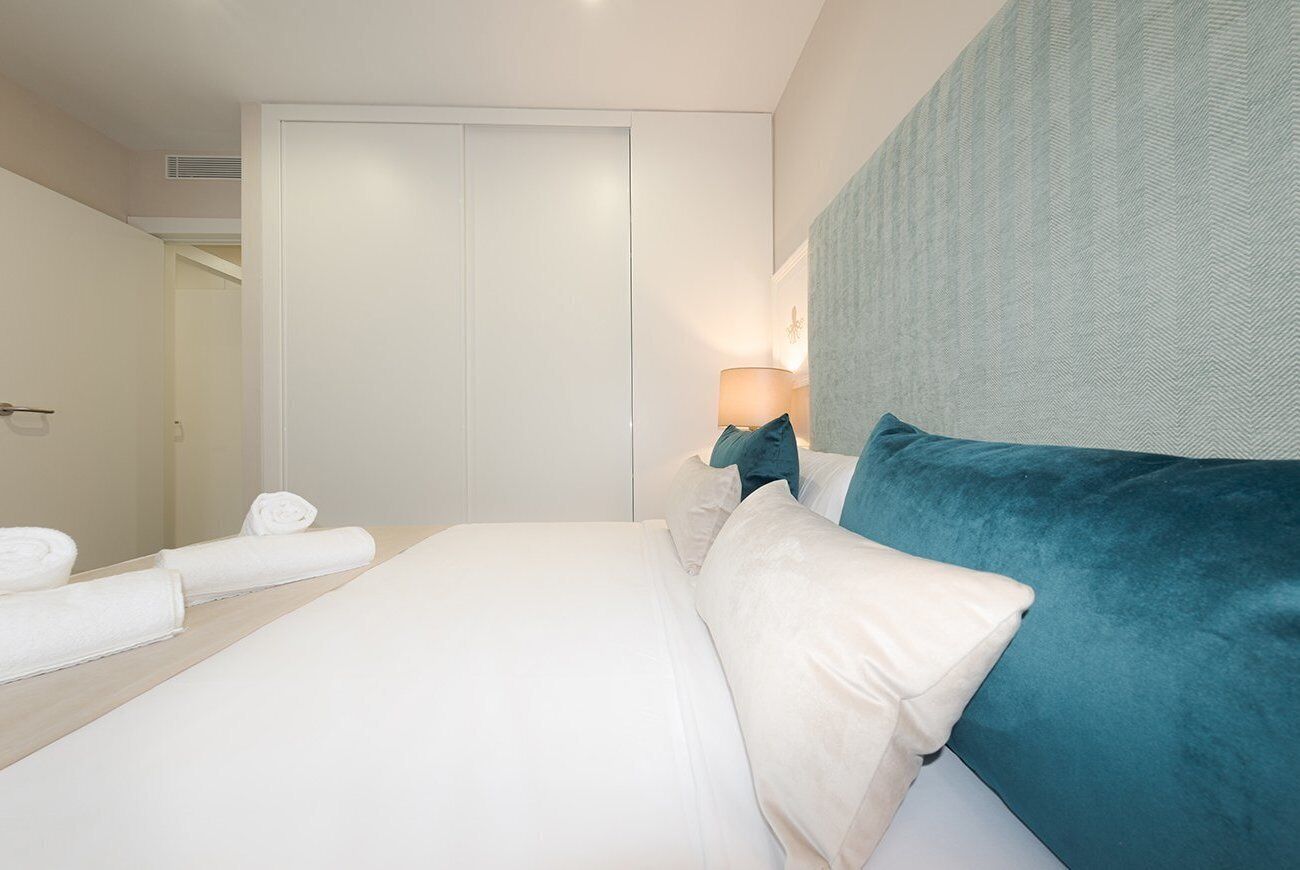 Un dormitorio con cama, mesita de noche, lámpara y puerta.
