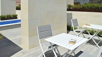 Un patio con mesas y sillas de metal blanco, una piscina pequeña y plantas en macetas.