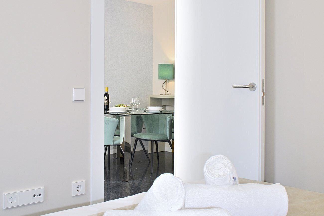 A hotel room with a bed, a bathroom, and a dining area visible through an open door.