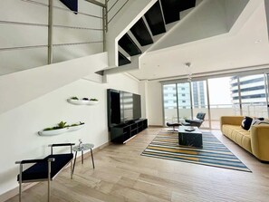 Un salon moderne avec un escalier, un téléviseur à écran plat, un canapé et une table basse.