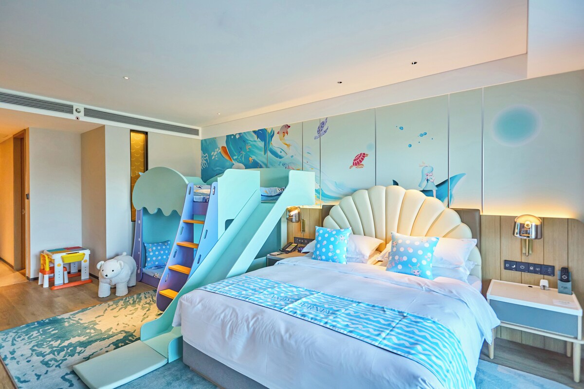 Un dormitorio infantil con un tobogán, una cama con edredón azul estampado y un mural de criaturas marinas en la pared.