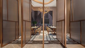 A modern hotel lobby with a central dining area, a large flat-screen TV, and a decorative chandelier. - Holiday Inn Quzhou by IHG (Quzhou)