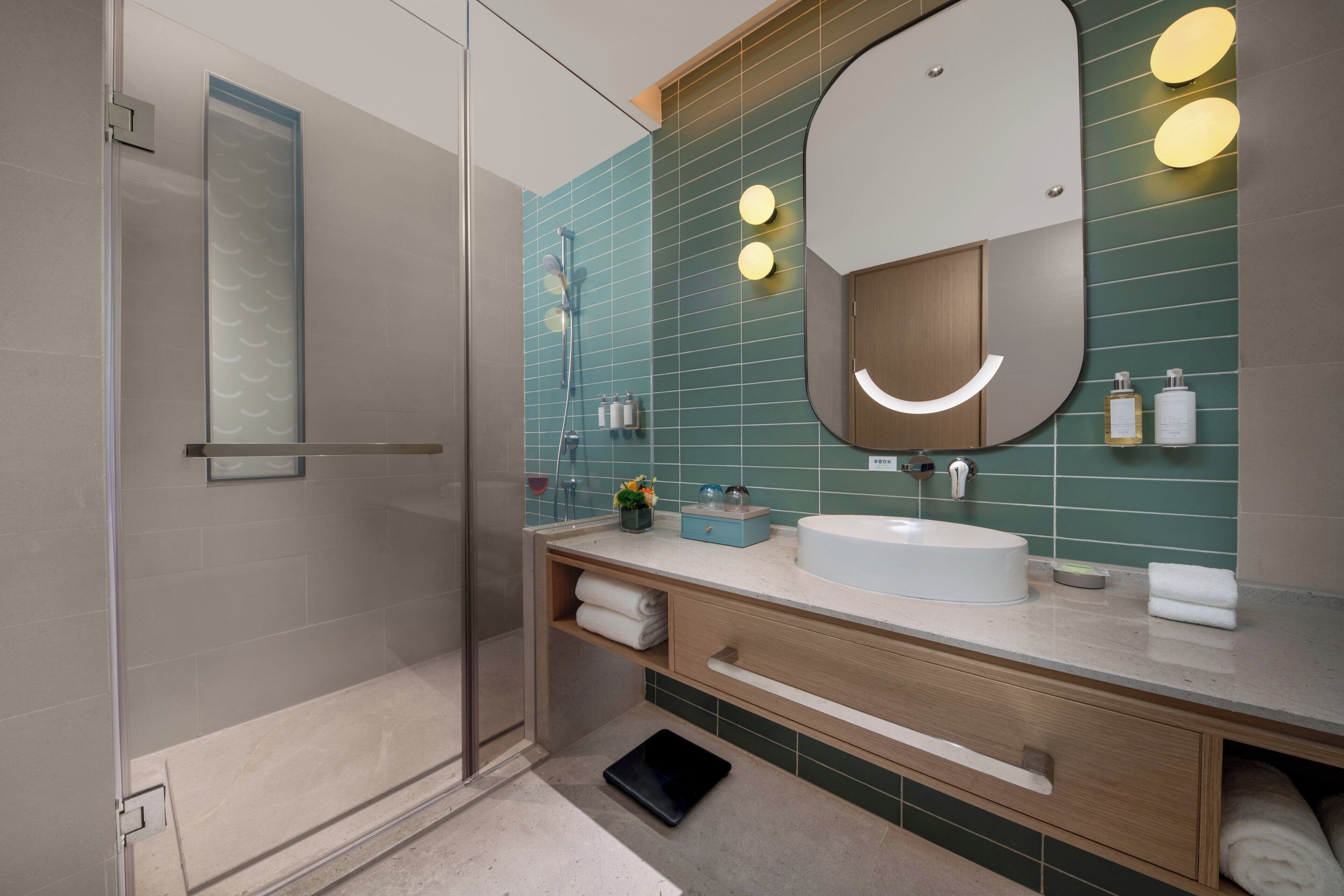 A modern bathroom with a glass shower enclosure, a white sink, and a vanity with a mirror.