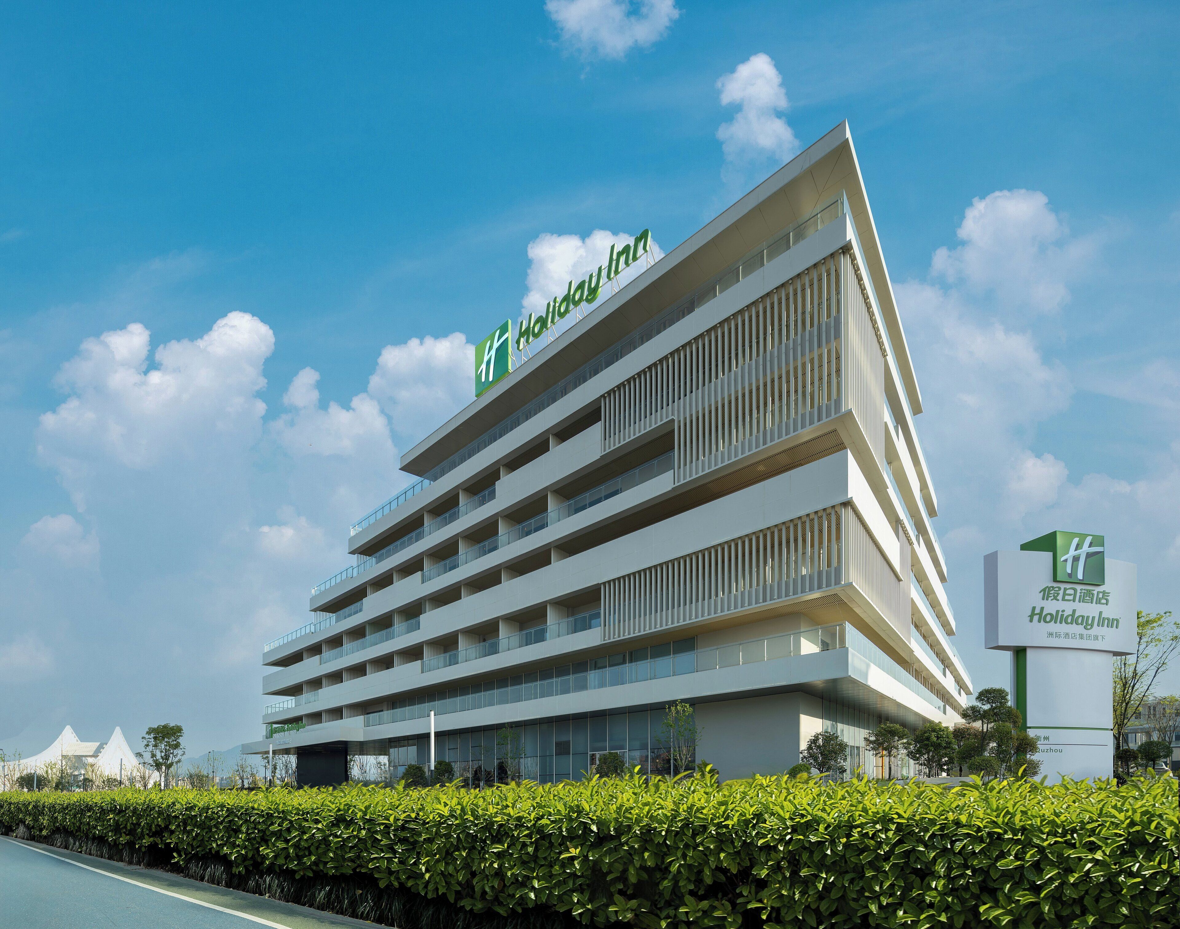 A modern hotel building with multiple floors and balconies, featuring a prominent sign for Holiday Inn.
