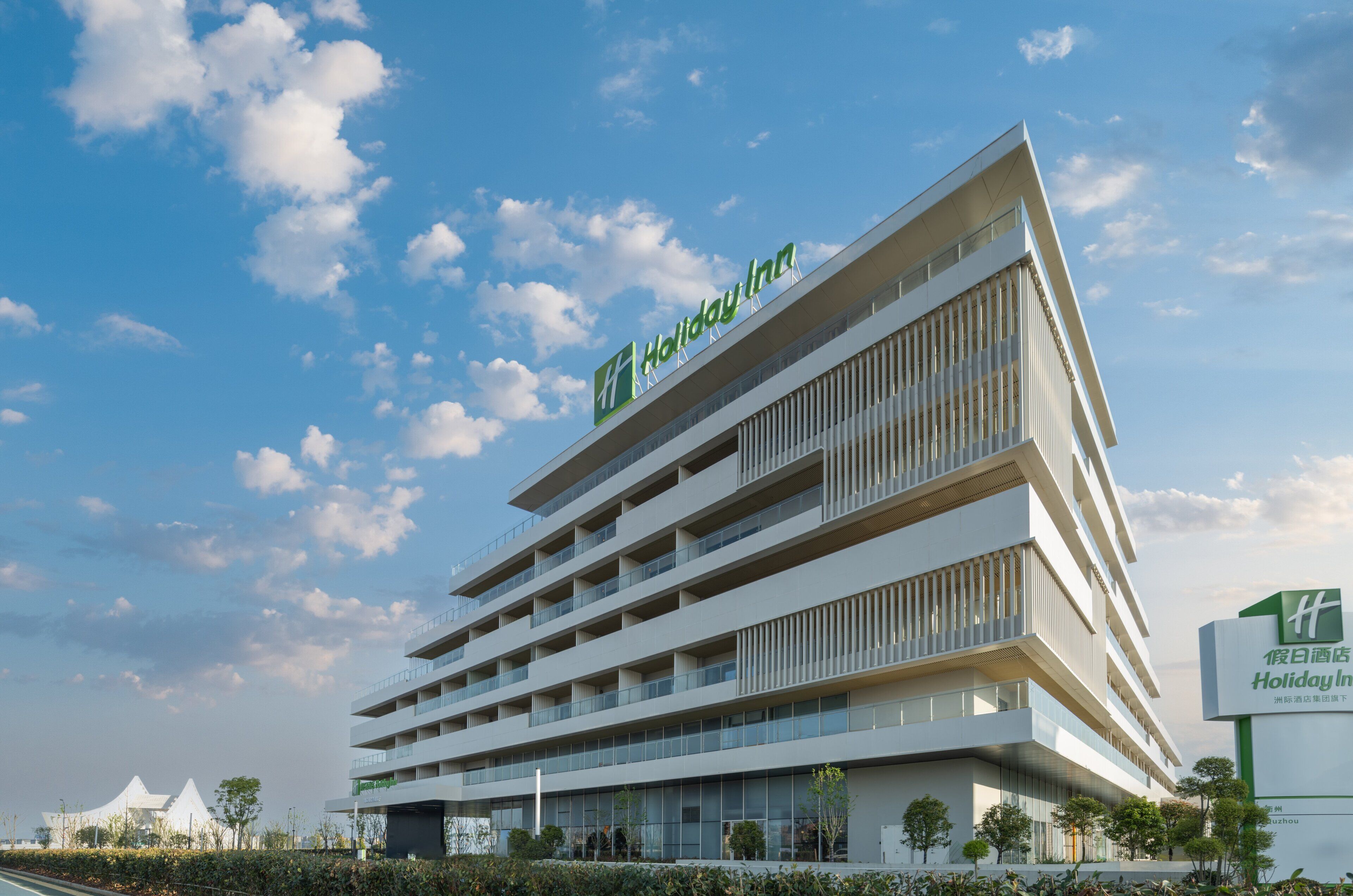 Un hôtel Holiday Inn à plusieurs étages, doté d’un design moderne, avec des balcons à chaque étage et une vue dégagée sur le ciel.
