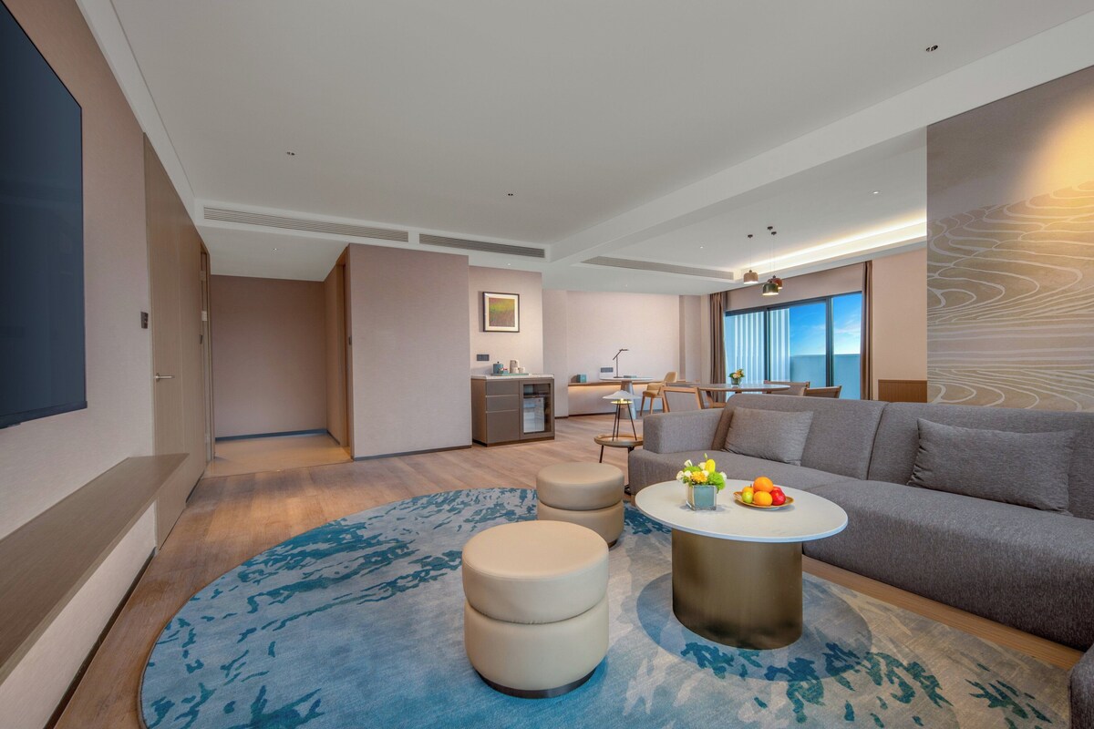 Una sala de estar moderna con un sofá gris, una mesa de centro redonda con fruta y una alfombra azul estampada.