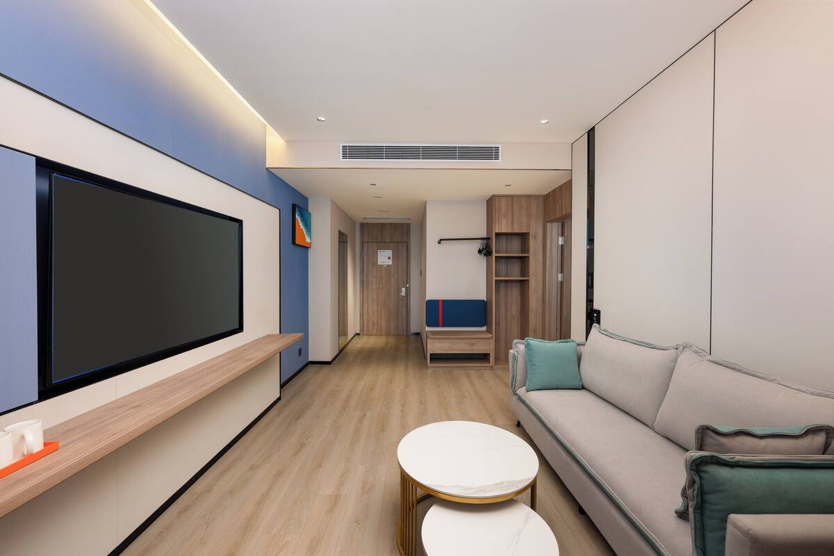 A modern living room with a flat-screen TV, a sofa, two small tables, and a bench.