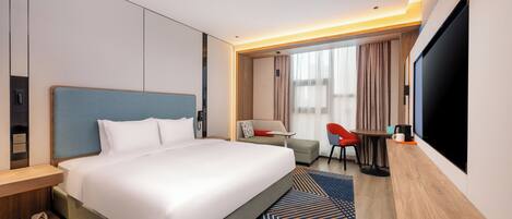 Ein Hotelzimmer mit einem großen Bett, einem Schreibtisch, einem Fernseher und einer Sitzecke mit Stuhl und Tisch.